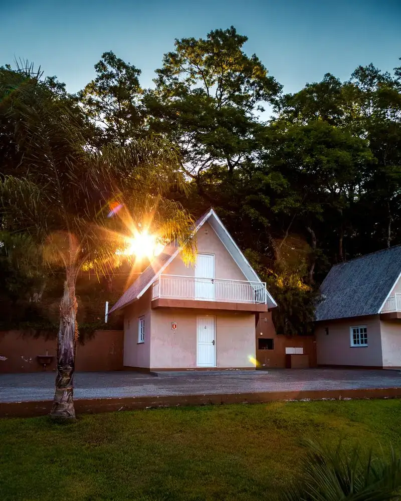Cabana em estilo chalé entre palmeiras, com o sol se pondo atrás