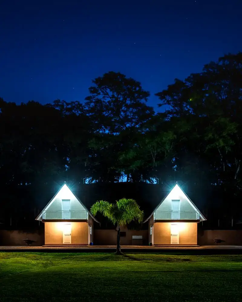 Duas cabanas iluminadas à noite, com uma palmeira entre elas