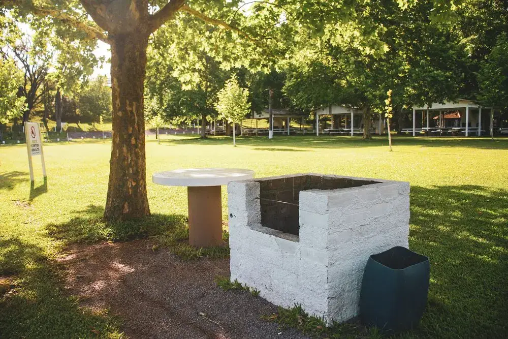 Churrasqueira de alvenaria branca com mesa redonda, no gramado