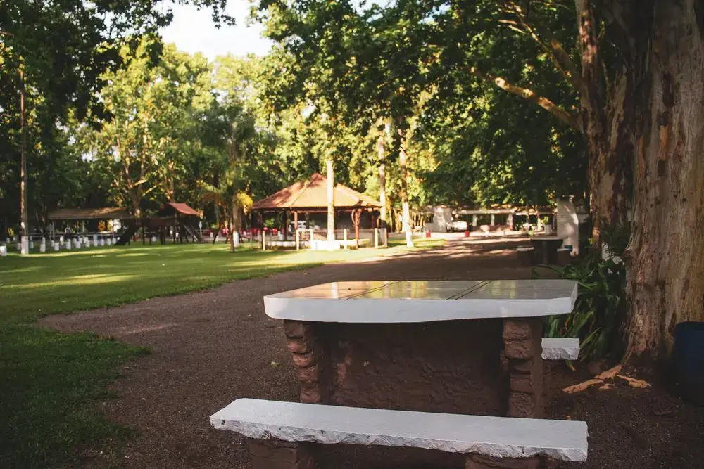 Mesa e bancos de pedra no bosque, com gazebos ao fundo