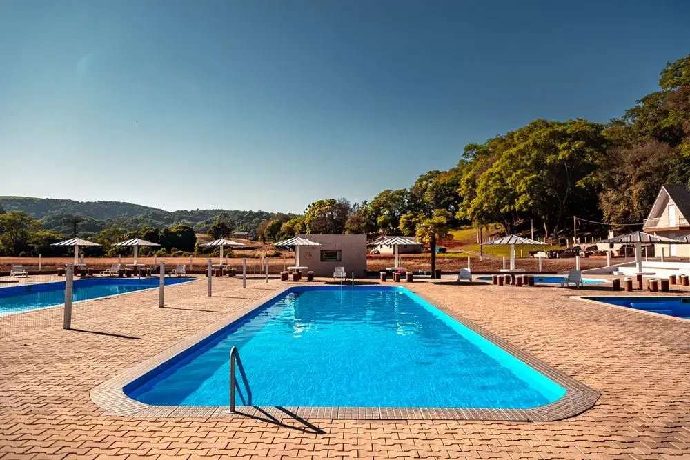 Piscina adulto com escada e deck de pedra, céu azul e morros ao fundo